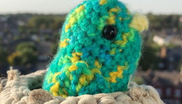 A picture of a crochet green bird sitting in a crochet nest