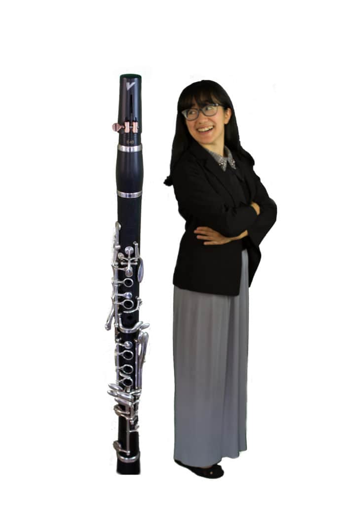 Image of Anna standing next to a clarinet as tall as she is